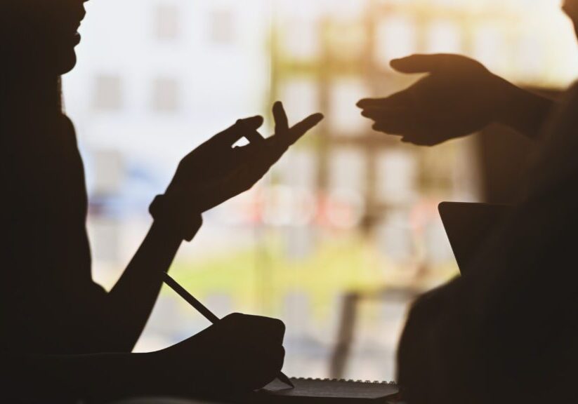 silhouette of young designer team standing with a white blank screen laptop and notebook in hands while discussing/talking about them new project with the modern office as background.